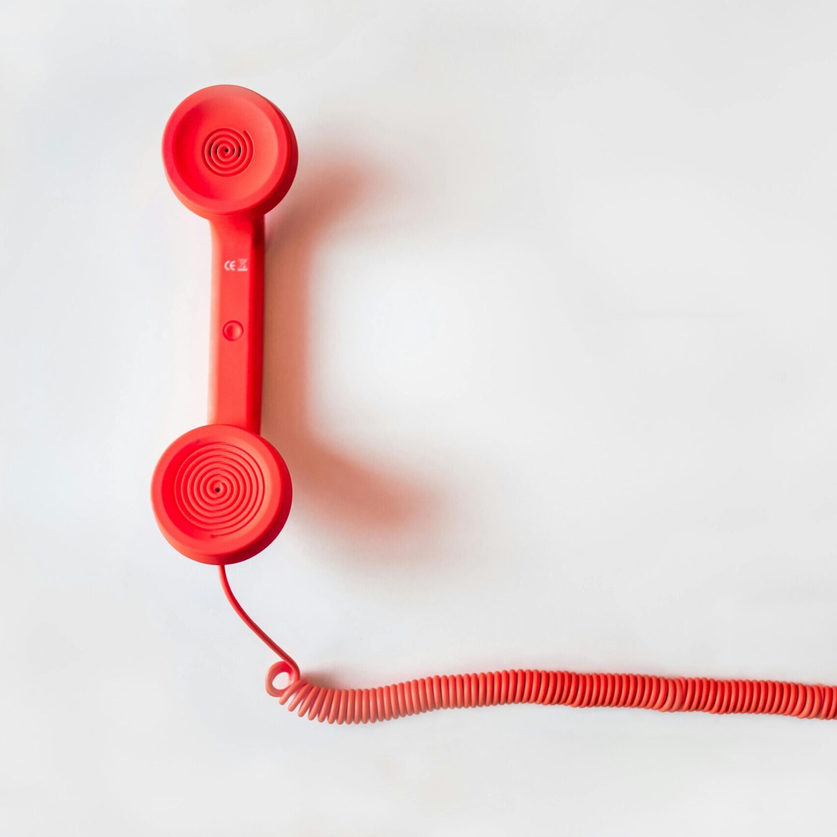 Vintage red phone handset with coiled cable on a clean white background, classic communication device.